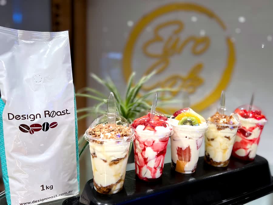 Dessert cups with berries and granola beside a bag of Design Roast coffee